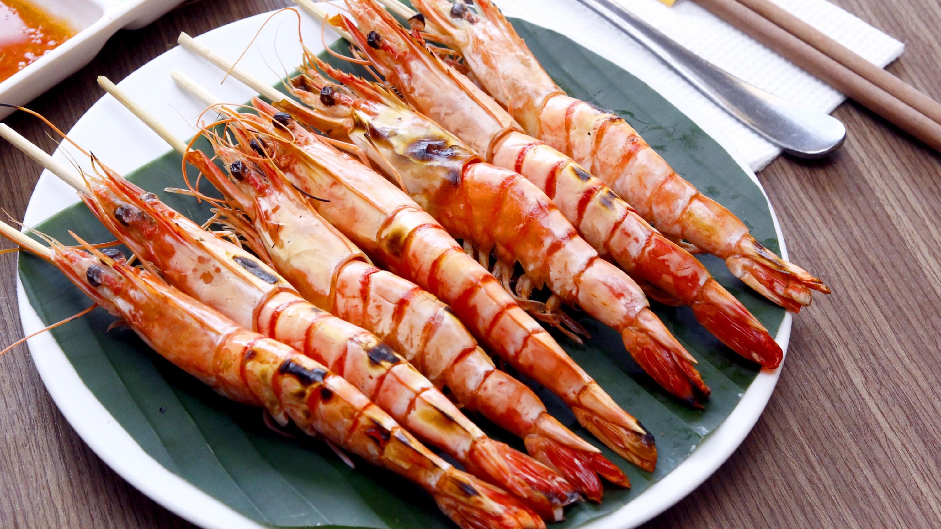 Xiên tôm nướng màu đỏ cam xếp gọn trên đĩa trắng lót lá chuối xanh