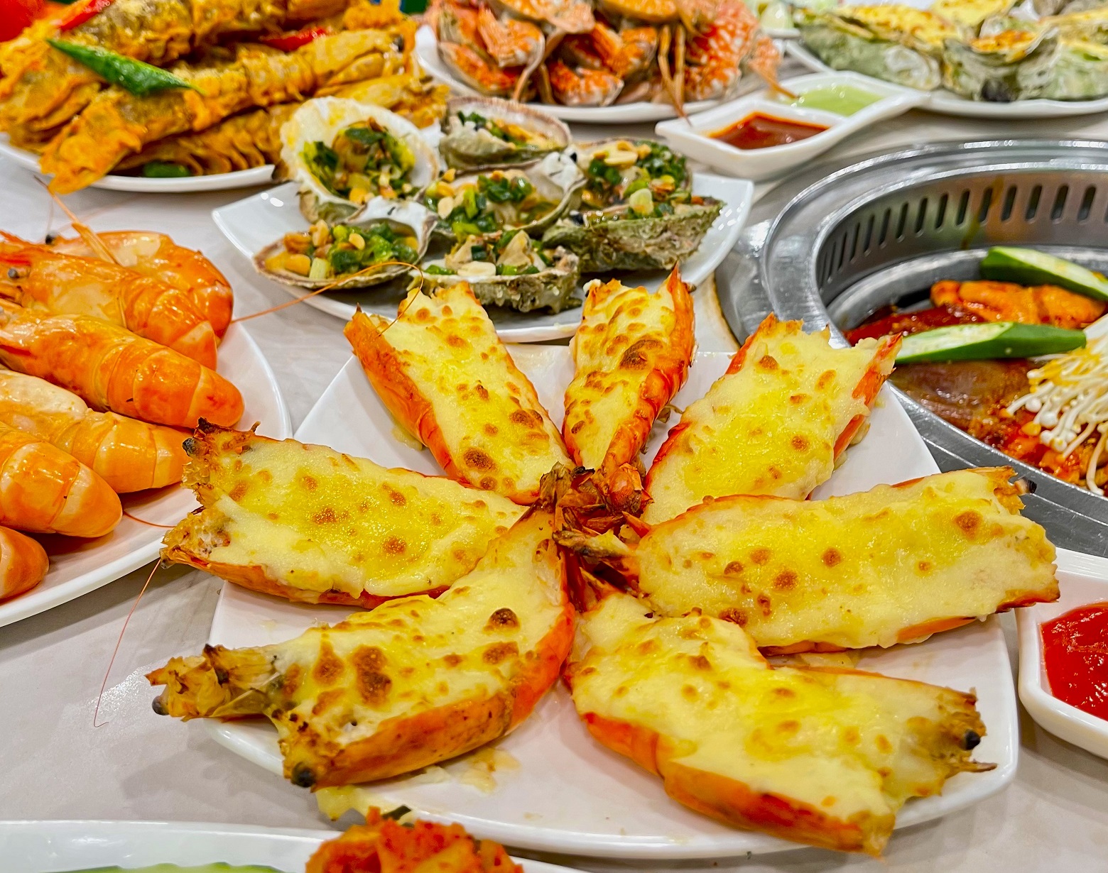 Đĩa tôm nướng phô mai cùng nhiều món hải sản chế biến sẵn như hàu nướng, tôm luộc trên bàn ăn.